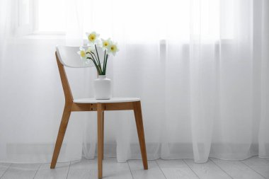 Beyaz odada çiçekli sandalye ve ışık perdeleri