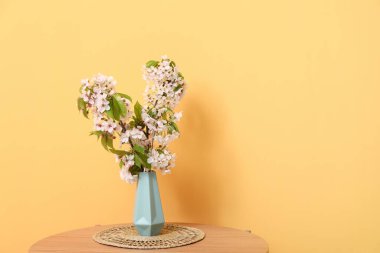 Turuncu duvarın yanındaki sehpanın üzerinde çiçek açan dalları olan vazo.