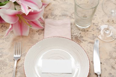 Tabak, çatal bıçak, bardaklar, peçete, yer kartı ve çiçeklerle dolu güzel bir masa.