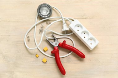 Beyaz ahşap arka planda pense, uzatma kablosu ve elektronik aletler.