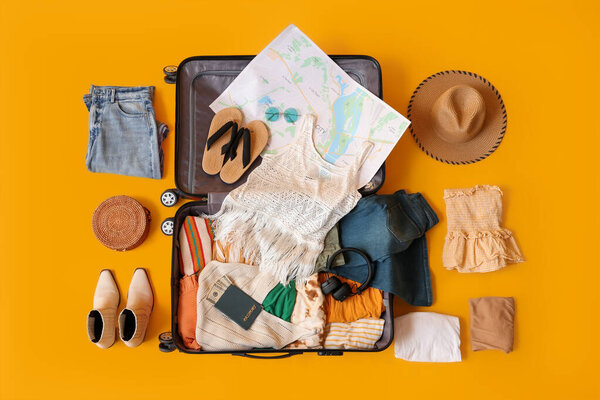 Открытый чемодан с женской одеждой, картой и паспортом на желтом фоне. Концепция путешествия