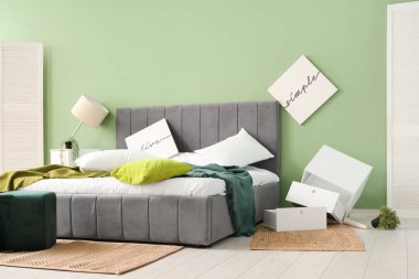 İçinde posterler ve ters çevrilmiş masa olan dağınık bir yatak odası.