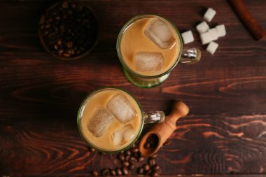 Bir bardak buzlu latte, içinde şeker küpleri ve ahşap arka planda kahve çekirdekleri.