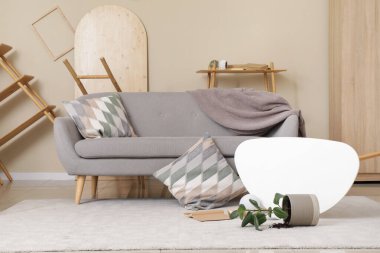 Hasarlı oturma odasının içinde kanepe ve depremden sonra mobilya devrilmiş.