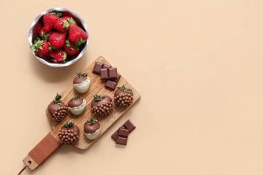 Çikolata kaplı çilekli ahşap tahta tahta ve kahverengi arka planda bir kase taze çilek.