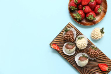 Çikolata kaplı çilekli ahşap tahta tahta ve mavi arka planda bir tabak taze çilek.