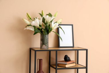 Odadaki bej duvarın yanında vazo dolusu çiçek ve fotoğraf çerçevesi olan raf ünitesi.