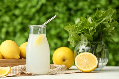 Dışarıdaki beyaz ahşap masada naneli bir şişe taze limonata ve vazo.