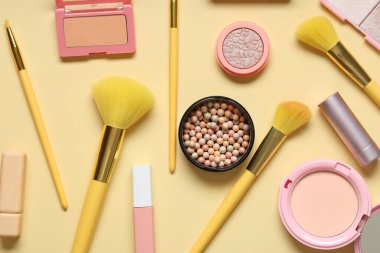 Sarı zemin üzerinde kozmetik ürünler bulunan şık makyaj fırçaları
