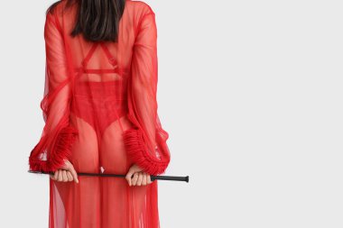 Gri arka planda seks dükkanından kırbaçlanmış iç çamaşırlı güzel bir kadın.