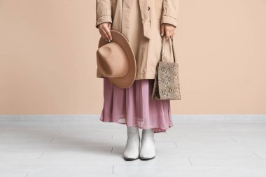 Elbiseli, ceketli, botlu, bej rengi duvarın yanında şık bir bayan.