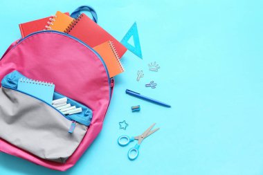 Mavi arka planda farklı kırtasiye malzemeleriyle modern okul sırt çantası.