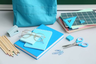 Okul çantasının içinde farklı kırtasiye malzemeleri ve beyaz masada gözlük var.