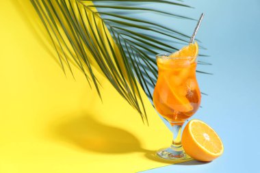 Renkli arka planda bir bardak Aperol spreyli kokteyl ve palmiye yaprağı.