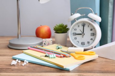 Gri duvara karşı ahşap masanın üzerinde alarm saati olan farklı kırtasiye seti.