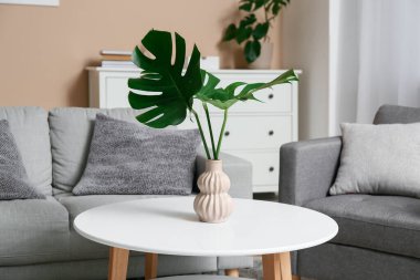 Masada ve şık koltukta tropikal canavar yaprakları olan modern bir oturma odası.