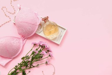 Sütyenli kompozisyon, bir şişe parfüm ve pembe arka planda aksesuarlar.