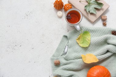 Sıcak süveterli kompozisyon, bir fincan çay, kitap ve açık arkaplanda güzel bir sonbahar dekoru.
