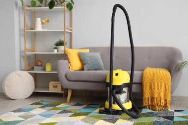Oturma odasındaki gri kanepenin yanındaki halıda modern elektrikli süpürge.