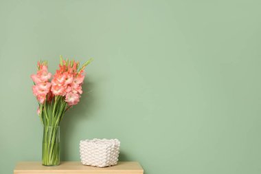 Yeşil duvarın yanındaki rafta gladiolus çiçekleri olan vazo.