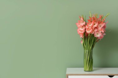 Yeşil duvarın yanındaki klozette gladiolus çiçekleri olan vazo.