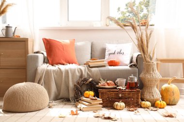 Çaydanlıklı sonbahar kompozisyonu, bir fincan sıcak içecek, lezzetli çörekler ve sepetli balkabakları oturma odasında.