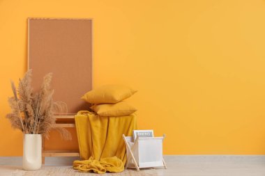 Yastıklı bank, otlar, kitap tutacağı ve odanın sarı duvarındaki çerçeve.