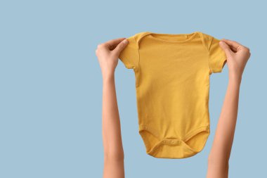 Mavi arka planda bebek tulumu olan kadın elleri.