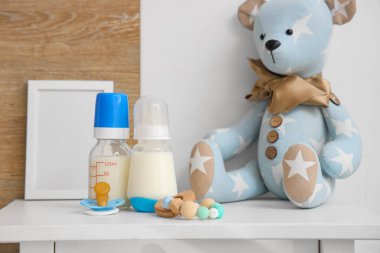Bebek sütü formülü, emzik, oyuncaklar ve açık komodinin üzerindeki boş çerçeve.