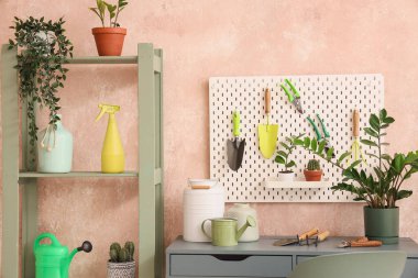 Bej duvarın yanında bahçe aletleri ve bitkiler var.