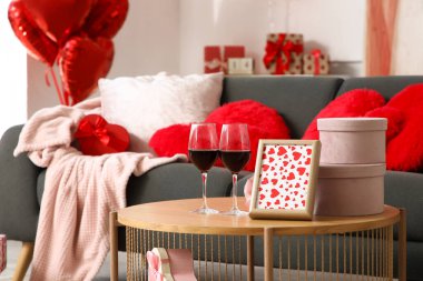 İçinde gri kanepe, kalp şeklinde yastıklar, balonlar ve hediye kutularının olduğu festival odasının içi. Sevgililer Günü kutlaması