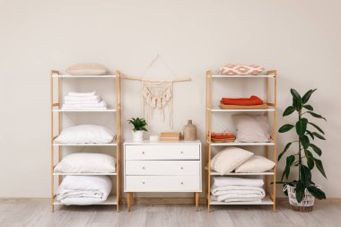 Beyaz duvarın yanında temiz çarşaflı, battaniyeli ve yastıklı raflar.