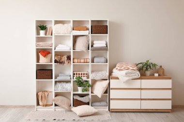 Raflarda temiz çarşaflar, sepetler ve beyaz duvarın yanında bitkiler var.