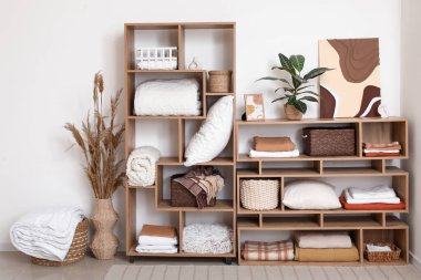 Odanın içindeki beyaz duvarın yanında temiz yatak çarşafları, ekose kumaşları ve yastıkları olan raf ünitesi.