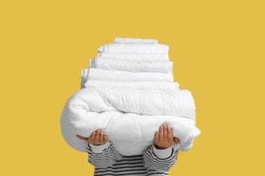 Sarı arka planda battaniye ve temiz çarşaf yığını olan genç kadın, yakın plan.