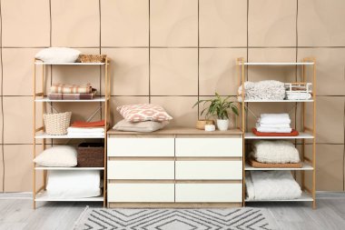 Temiz çarşaflar, battaniyeler ve yastıklar, oda içindeki bej döşeme duvarının yanındaki raf ünitelerinde.