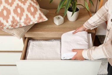 Genç bir kadın, temiz çarşaf yığınını odadaki çekmecelerin arasına koyuyor.