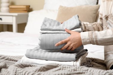 Yatak odasında temiz çarşaf yığını olan genç bir kadın, yakın plan.