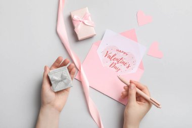 Elinde gri arka planda hediye kartı olan kalem ve zarf tutan bir kadın. Sevgililer Günü kutlaması