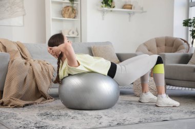 Sportif genç bayan evde spor topu egzersizleri yapıyor.