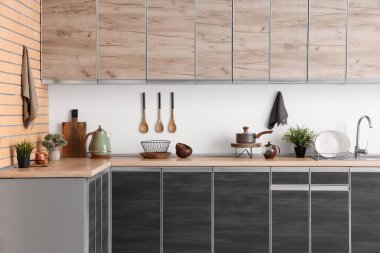 Beyaz duvarın yanında siyah tezgah ve çatal bıçakları olan modern mutfağın içinde.