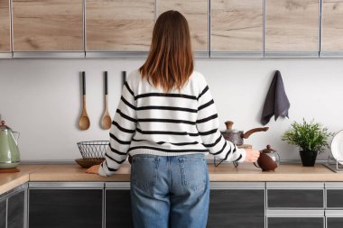 Evde mutfak tezgahlarının yanında çaydanlığı olan genç bir kadın.