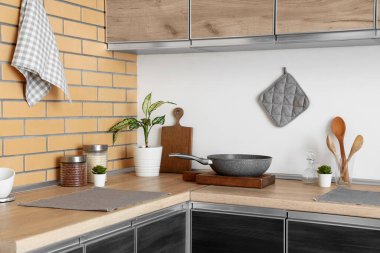 Mutfaktaki masada tava, çatal bıçak ve bitkiler var.