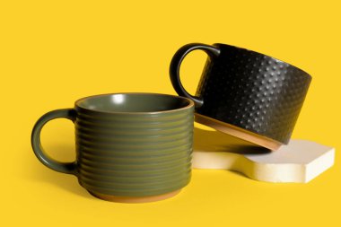 Sarı arka planda sıva podyumu olan farklı seramik kupalar.