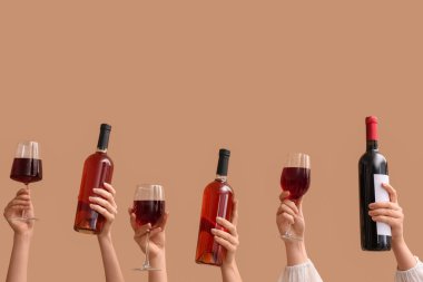 Şişeli kadın elleri ve bej arka planda kırmızı şarap bardakları.