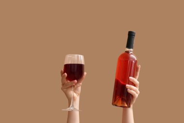Şişeli kadın elleri ve bej arka planda bir bardak kırmızı şarap.