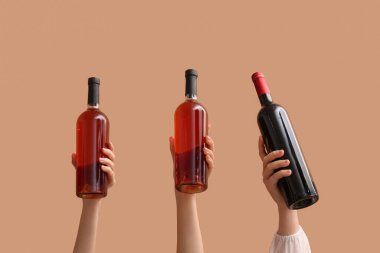 Bej arka planda kırmızı şarap şişeleri olan kadın eller.