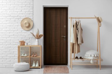 Koridorun içinde ayakta duran ayakkabılar ve beyaz duvarın yanında giysi olan askılar.