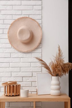 Vazo ve fotoğraf çerçevesi koridorda beyaz tuğla duvarın yanındaki masada.