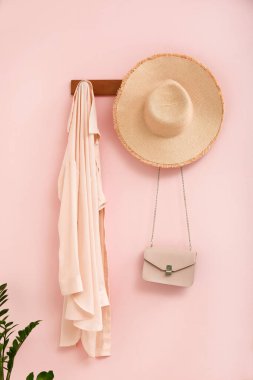 Koridordaki pembe duvarda şapkalı, çantalı ve elbiseli askı